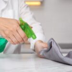 Woman cleaning white solid surface with cloth and detergent indoors, closeup