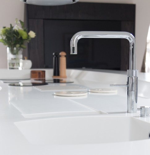 A silver tap and sink with white Corian solid surface material